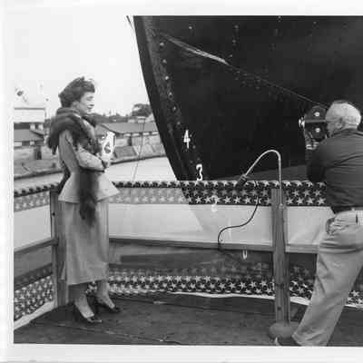 Woman holding christening bottle and man with film camera at launching of Badger September 6, 1952
