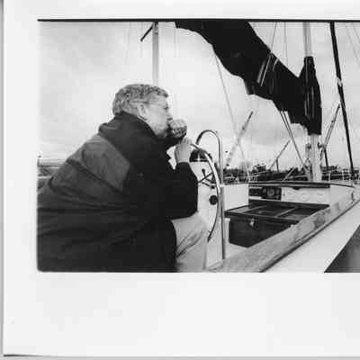 Man resting on wheel of sailboat with barges in background