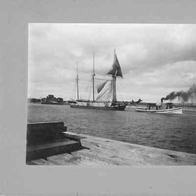 Tug towing tall ship with 3 sails through channel