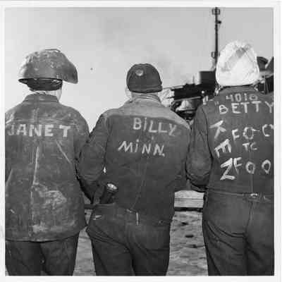 Janet, Billy Minn, and Betty, in welders jackets with backs turned to camera
