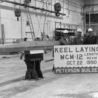 4 men in hard hats with sign saying "Keel laying MCM-12" 1990