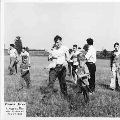 Man holding pig next to kid with gun at SBSB&DD Co. 1st annual picnic August 22, 1943