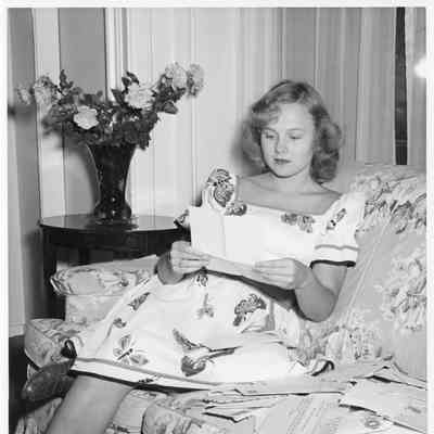 Patsy Smith wearing a dress sitting on couch reading a letter