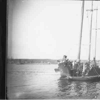 Three-masted vessel with sails down docked next to dock loaded with lumber