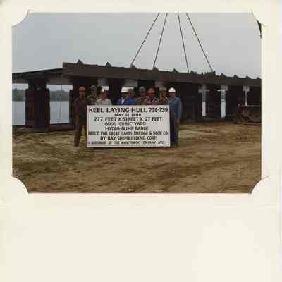 Crew of 9 men standing in back of sign for Keel laying Hull-738-739 1986