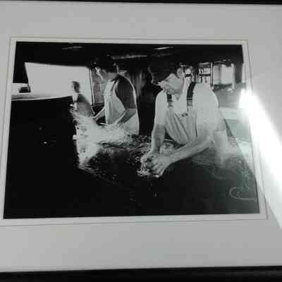 Framed photograph of three fishermen unloading big mesh aboard Freitag