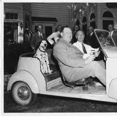 two men in sports car, dalmatian dog sitting in back