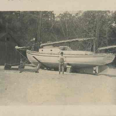 Boy stands next to beached sailboat Cora Belle