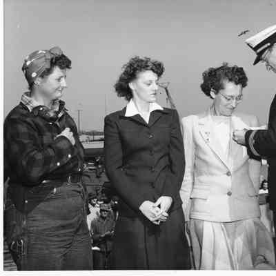 Three women and officer at ceremony with crowd in background