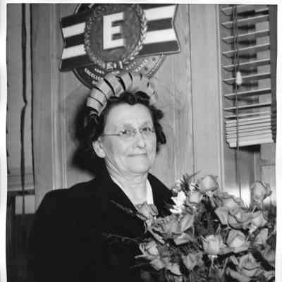 Mrs. Jos. O'Boyle holding roses in front of E plaque