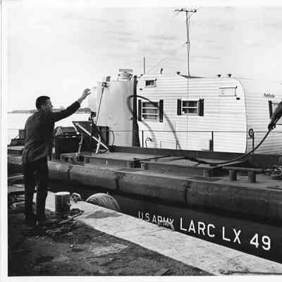 Man pulling in rope while standing on US Army Larc LX 49 with camper inside