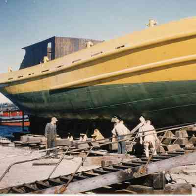 Green and yellow ship with 5 men working on ground