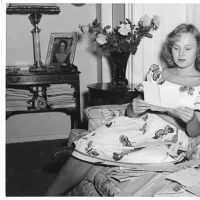 Patsy Smith wearing a dress sitting on couch reading a letter