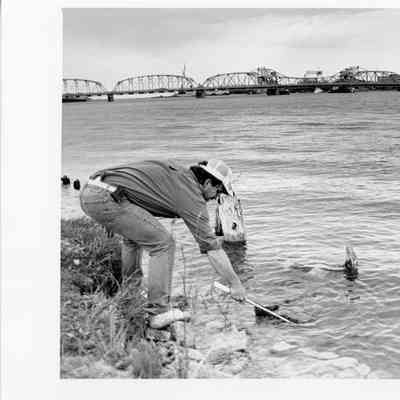 man with beeper bending over netting something with Michigan Street bridge 1993