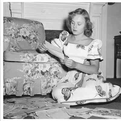 Patsy Smith wearing a dress sitting on floor reading a letter