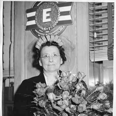 Mrs. Jos. O'Boyle holding roses in front of E plaque