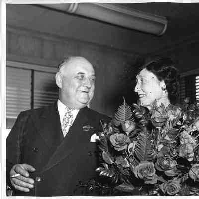 Mrs. W. H. Gallieane holding roses alongside smoking man