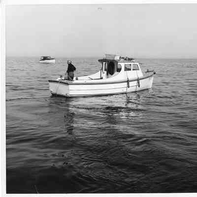 Two boats in the open water with man is standing on the stern of the boat