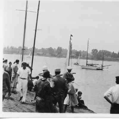 people on dock watching sailboats in water