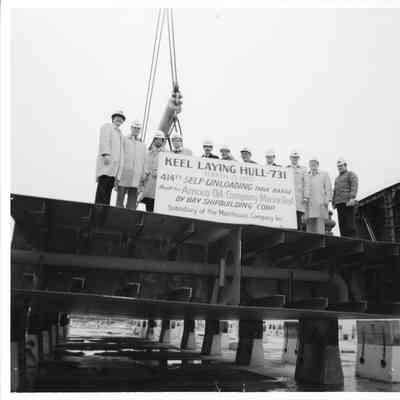 Men wearing hard hats behind large sign for Hull 731 Self-Unloading tank barge
