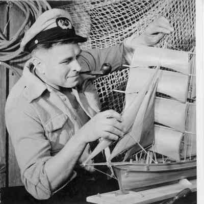 Man fixing mast on vessel model with pipe in mouth