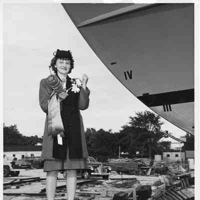 Lucille Gast holding bottle of champagne by bow of vessel