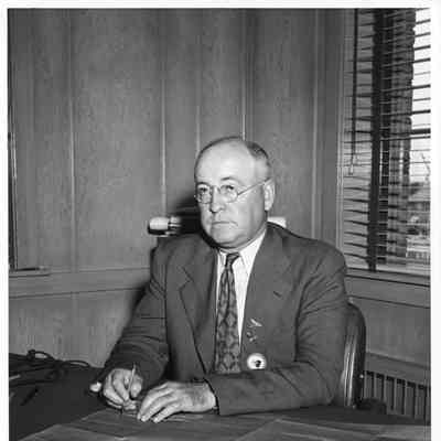 Leathem D. Smith seated at his desk with a blueprint and pencil