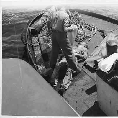 Two men standing over a corpse on a boat