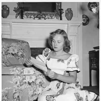 Patsy Smith wearing a dress sitting on floor reading a letter