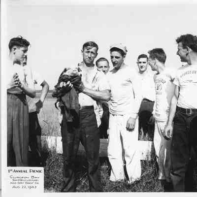 Group of men with one holding a pig at SBSB&DD Co. 1st annual picnic August 22, 1943