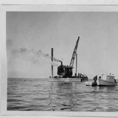 Crane operating on barge in open water with tugboat nearby