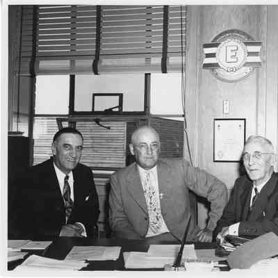 Leathem D. Smith and two men seated at desk in office