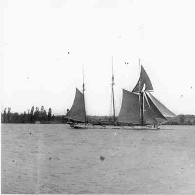 Three-masted sailing vessel with farmland in the background