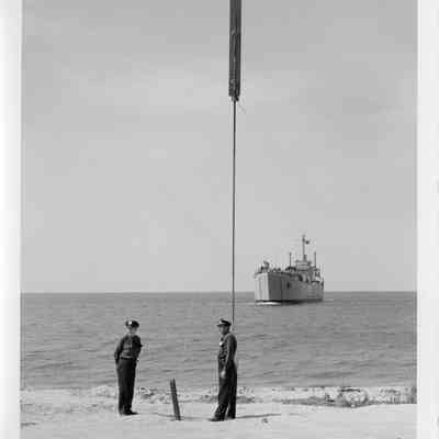 Two men on shore with LST-1166 behind in water