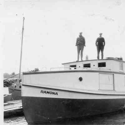 Two men standing on pilot house of fishing tug Ramona while docked