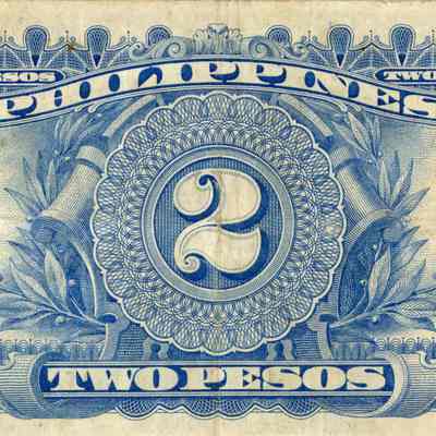 Back, or reverse, side of the two pesos bill. Slight fold creases are visible within the bill.: The image depicts the back of a vintage two-peso currency bill from the Philippines. The bill is a light, cream color with blue designs. At the center, a large numeral "2" is prominently displayed within an elaborate circular frame that is set against a leafy vine and plaque. The words "TWO PESOS" appear in banners above and below the central design, with additional "2" numerals in varying decorative frames at each corner.