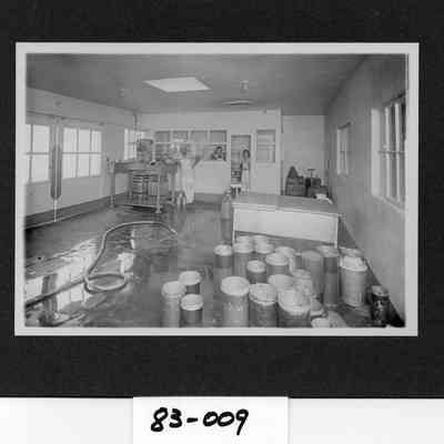 Twin City Creamery one of the work rooms.  Pictured are milk cans and barrels, Own Kinneman, Gertrude Hedington, and Louise Schaffner, Turner.