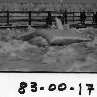 Four men, No ID's, standing on wooden platform (bridge, ferry dock?) that juts out onto the river.  River is jammed with large chuck of ice.  With snow-covered bluffs in background.  Good photo of frozen river.