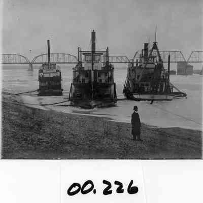 W.R. Todd, Mountain Gem, and Wallowa Steamboats at Kennewick landing. railroad bridge in background, Ice on river. Two unidentified men (one on shore, one on Wallowa with ice skates.)
