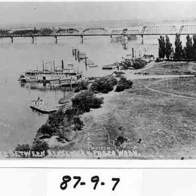 Two unidentified sternwheelers and a ferry at the Kennewick docks railroad bridge in backgrouind