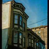          Color slide of close-up view of row house façades, cornices, brackets and bay windows including storefront signage reading 