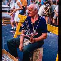 Color slide of a man sitting on a crate at a street fair.