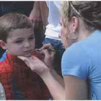 Color photo of a boy getting his face painted by a woman at Biggie