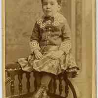 Sepia-tone photo of a boy seated on the arm of a corner chair in studio, Hoboken, n.d., ca. 1880-1885.