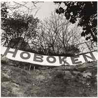 B+W photo of a hand-painted "Hoboken" sign attached to a fence probably above River Road, Hoboken, no date, [1976].