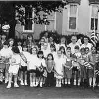 B+W group photo of of Hoboken Girl Scouts with flags standing in street, Hoboken, no date, ca. 1980-1985.