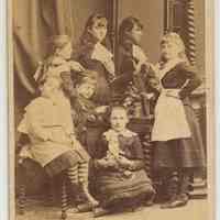 Sepia-tone photo of 6 girls in a domestic pose with furniture, Hoboken, n.d., ca. 1880-1885.