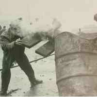 B+W photo of "On the Waterfront" filming in Hoboken: an unidentified man near smoking metal barrel, Hoboken, n.d., ca. late 1953-early 1954.