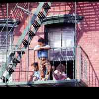 Color slide of three children on the fire escape of a brick building.