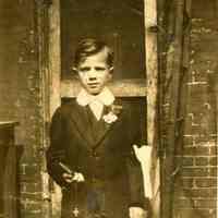 B+W photo of Billy Harriot on his first communion standing in front of door to a house on Willow Terrace, Hoboken, no date, ca. 1935-1940.